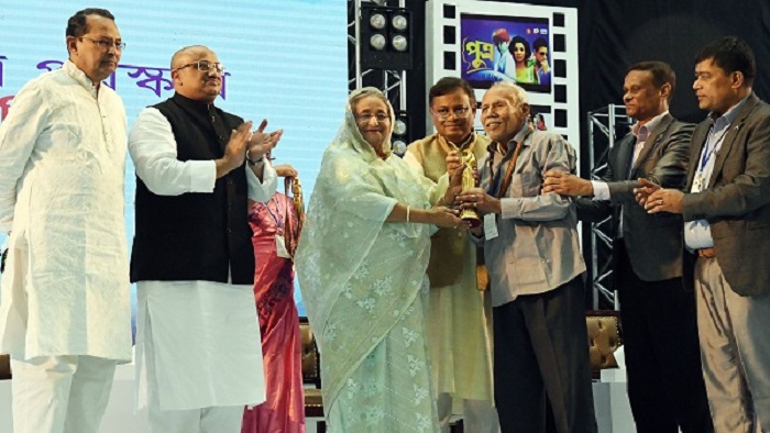 প্রধানমন্ত্রী শেখ হাসিনা জাতীয় চলচ্চিত্র পুরস্কার ২০১৭ ও ২০১৮ প্রদান অনুষ্ঠানে চলচ্চিত্র অভিনেতা এ টি এম শামসুজ্জামানকে আজীবন সম্মাননা পুরস্কার প্রদান করেন। -ছবি: সংগৃহীত প্রধানমন্ত্রী শেখ হাসিনা জাতীয় চলচ্চিত্র পুরস্কার ২০১৭ ও ২০১৮ প্রদান অনুষ্ঠানে চলচ্চিত্র অভিনেতা এ টি এম শামসুজ্জামানকে আজীবন সম্মাননা পুরস্কার প্রদান করেন। -ছবি: সংগৃহীত